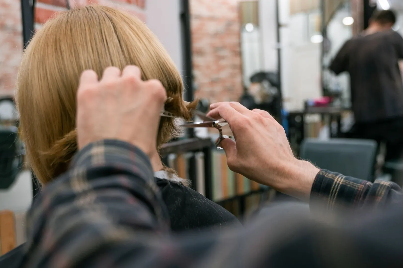 Stylist working on a client's hair in a warm brick-walled salon