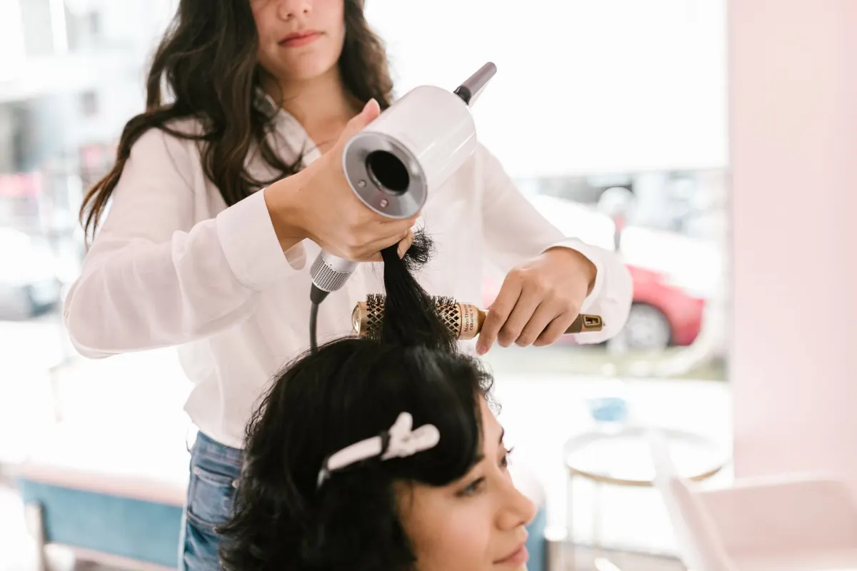 Stylist finishing a client's updo against a blush pink wall