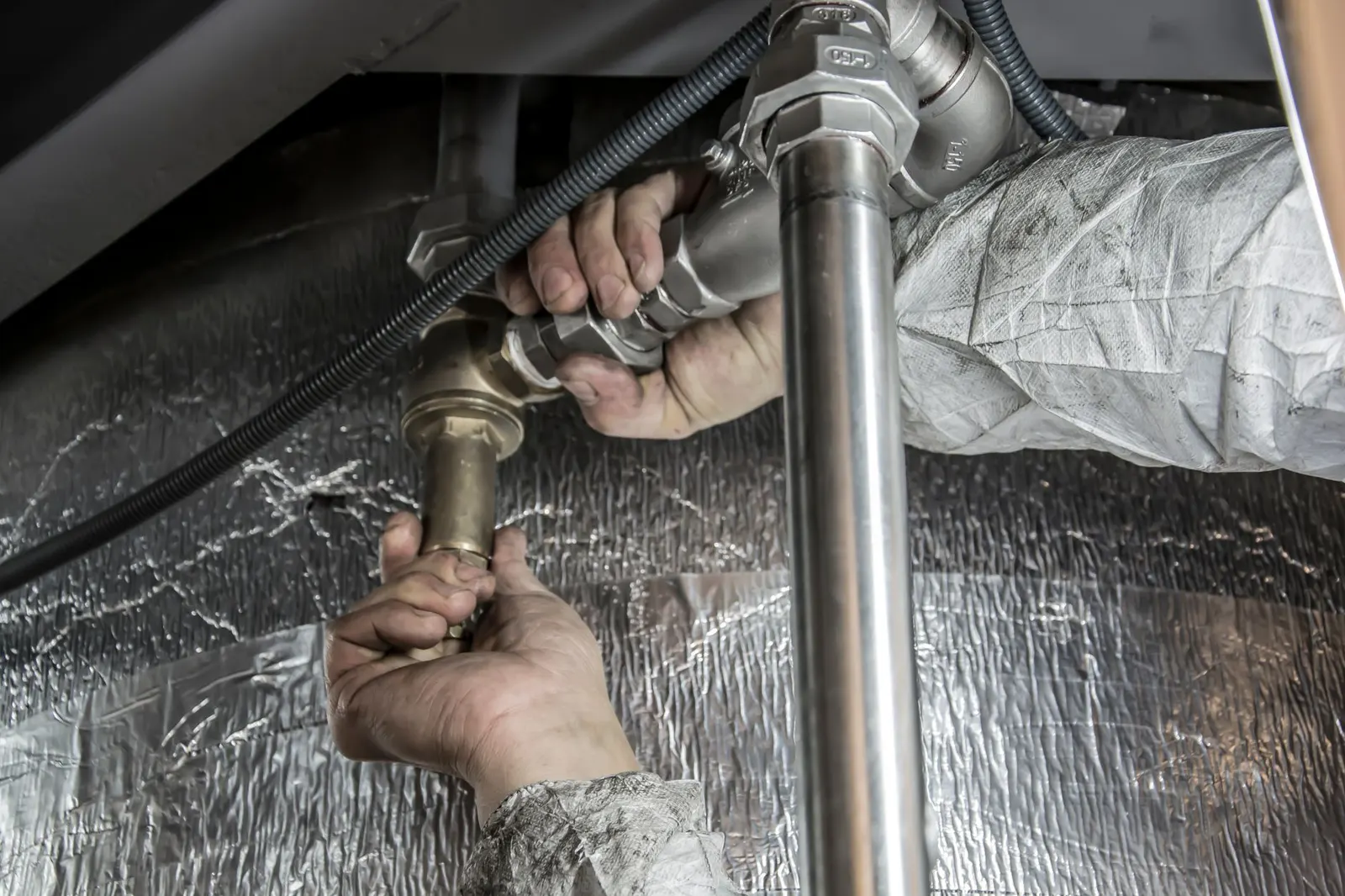 Plumber tightening an overhead supply line with a pipe wrench
