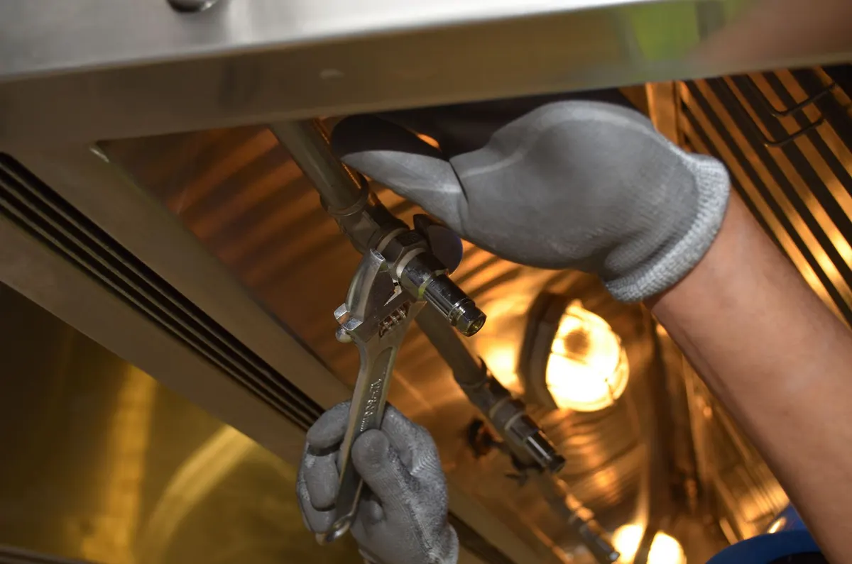 Gloved hand repairing a drain trap under a sink with an adjustable wrench